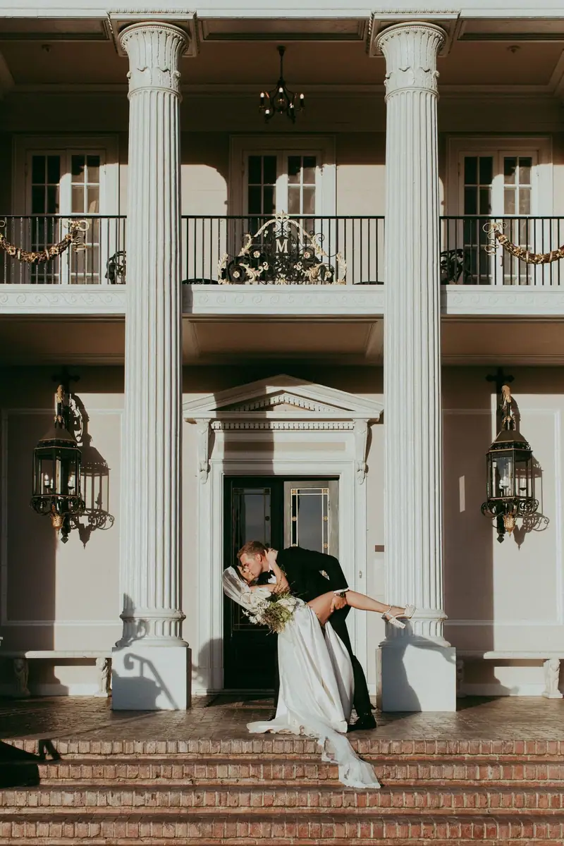 Bride and groom kissing on the brick steps of a white-columned home